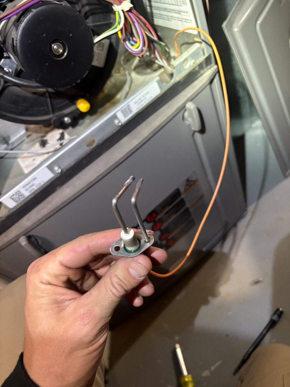 A furnace spark ignitor removed during a no-heat repair, with its twin electrodes and high-voltage wire